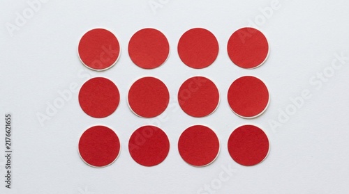 Set of red round adhesive paper stickers arranged in grid pattern on white surface top-down view natural lighting clean aesthetic