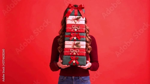 Woman Holding Tall Stack of Wrapped Christmas Gifts on Red Background, Festive Present Tower