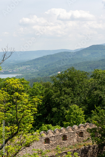 Obraz na płótnie Historic stone battlements of Chojnik Castle surrounded by green forest with mountain ridges and cloudy sky in the distance