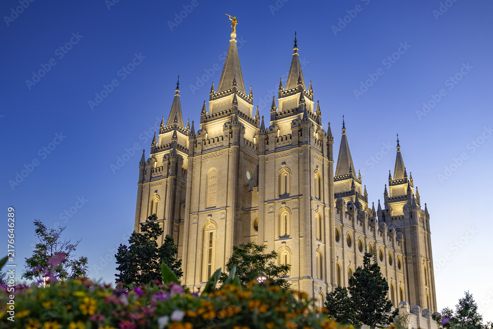 Obraz premium Salt Lake Temple at sunset, beautifully illuminated against a colorful evening sky, showcasing the iconic granite architecture, distinctive towers, and peaceful grounds of this historic Latter-day Sai