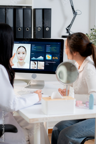 Young asian woman doctor consulting with woman patient in aesthetic clinic during looking at computer screen artificial intelligence software for beauty facial skin analysis diagnostic result.