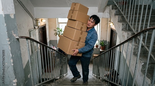 Man carrying heavy stack of cardboard boxes up apartment building stairs