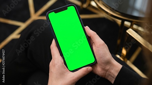 Person holding a smartphone with a green screen in a modern setting with gold accents