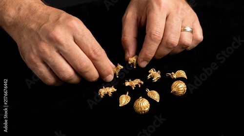 Close up of hands arranging small golden animal charms and pendants on a black background
