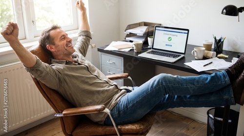 Man celebrating successful online shopping purchase with arms raised in victory at his desk