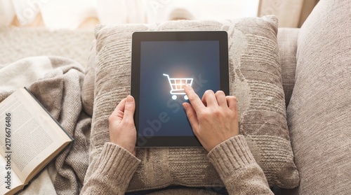 Person using tablet to shop online with shopping cart icon on screen