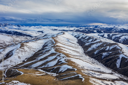 Foto Aerial view of snow-dusted rolling mountain ranges under an overcast sky, showing exposed dry terrain