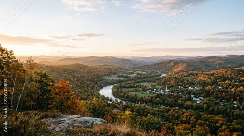 A stunning panoramic view showcases a vast, rolling landscape during the golden hour. The foreground features a rocky outcrop with trees displaying vibrant autumn foliage.