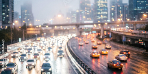 A busy city highway illuminated by traffic lights and buildings in rainy weather. Cars are moving through the wet streets, reflecting lights.