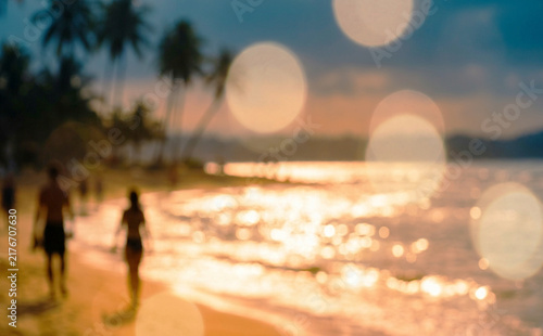 A beautiful beach scene at sunset, with silhouettes of people walking along the shore. Soft bokeh effects enhance the tranquil atmosphere.