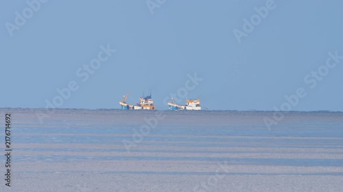 Fishing boats floating on distant ocean horizon under clear blue sky with heavy atmospheric heat haze mirage distortion in telephoto shot.