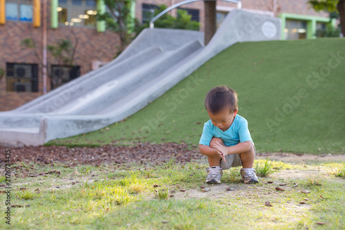 Toddler squatting on ground near playground slide outdoors