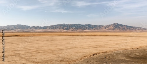 Vast wide angle landscape of a dry desert plain with distant mountains under a pale blue sky