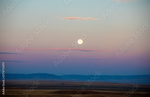 Bild auf Leinwand Full moon setting over open plains and distant mountains during pastel dawn sky