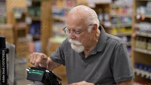 Photography An elderly man is shopping at a grocery store, using a card to check out his items