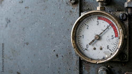 A close-up shot of an industrial pressure gauge, with its needle pointing to a red zone on the dial, mounted on a weathered metal surface, evoking a sense of raw utility and mechanical function.