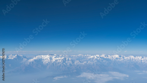 Beautiful mountain landscape. View from a height, from an airplane. Snow-capped peaks of the majestic Himalayas against the blue sky. There is fog and haze in the valley. Nepal.