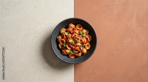 Top-down view of a bowl filled with authentic pasta al sugo featuring orecchiette noodles and fresh basil garnishes on a split tone textured surface.