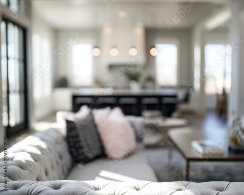 Modern Living Room Serenity: A bright, airy living room with a plush sofa, soft cushions, and a glimpse of a modern kitchen, bathed in natural light, evokes a sense of comfort and stylish living.