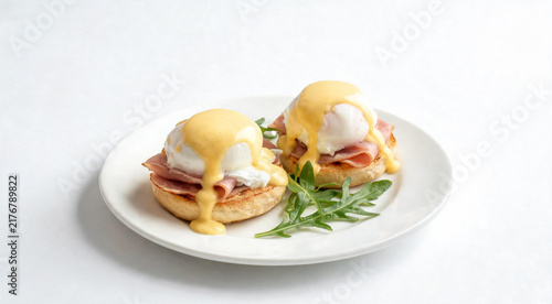 Eggs Benedict with hollandaise sauce on white plate over pure background