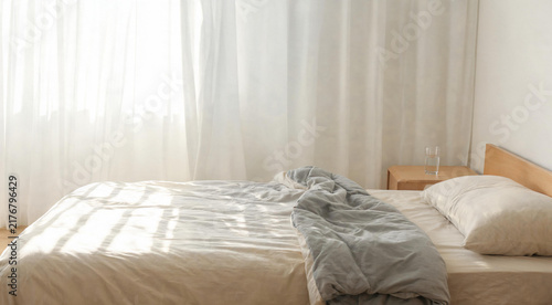 Morning sunlight through sheer curtains casting stripes on white bed sheets