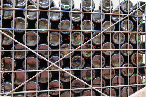 Dark glass wine bottles stacked horizontally in a metal storage cage at a winery, showing bulk bottle storage, maturation and traditional wine production.
