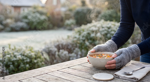 Hands in fingerless gloves holding a warm bowl of soup at an outdoor table