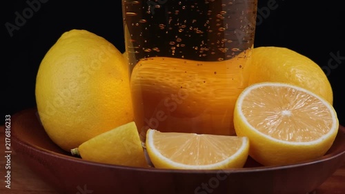 Fresh lemon juice being glass with lemons on table black background