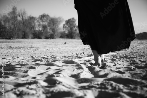 Canvas Print A woman in a long black dress walks barefoot on sandy beach