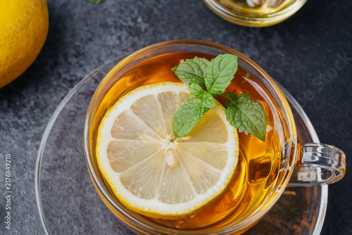 Quadro su tela Hot tea with lemon slice and mint leaves in a clear cup on a dark background
