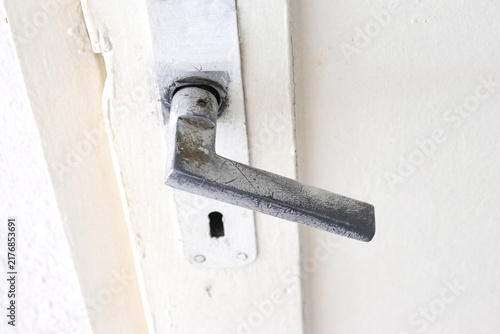 The worn metal handle of the white room door. Old door lock. Home or office entrance equipment. No people, nobody. Horizontal photo.
