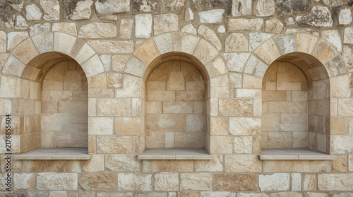 Stone wall with three arched alcove niches in warm neutral masonry texture