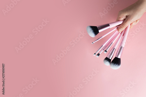 Foto A hand holds set of various pink-handled makeup brushes, fanned out against a soft pink backdrop, ready for flawless application