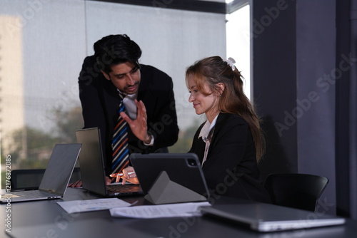 Photography Businessman raises an open palm making a decisive point to the amused seated colleague whose tablet glows on its stand at the daylit corner workstation in a bright modern coworking office