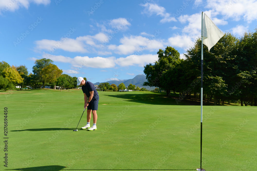 Obraz premium Man putting golf ball on green course near hole.
