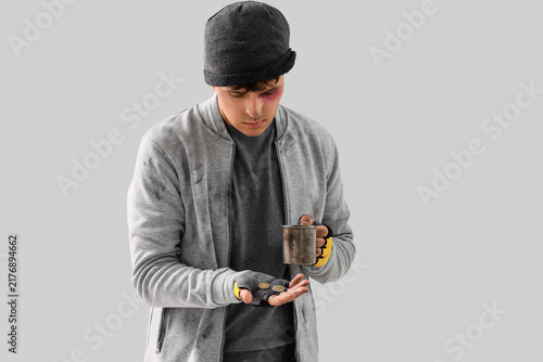 Cuadro en lienzo Young homeless man with cup and coins on light background