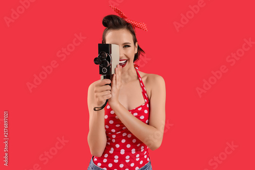 Beautiful young happy pin-up housewife with retro video camera on red background