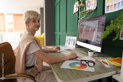 Young female graphic designer working with computer at table in office