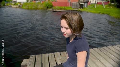 Girl sitting on a pier. Rear view Beautiful brunette girl with long hair sits on a wooden pier outdoors and looks into the distance while relaxing in nature.