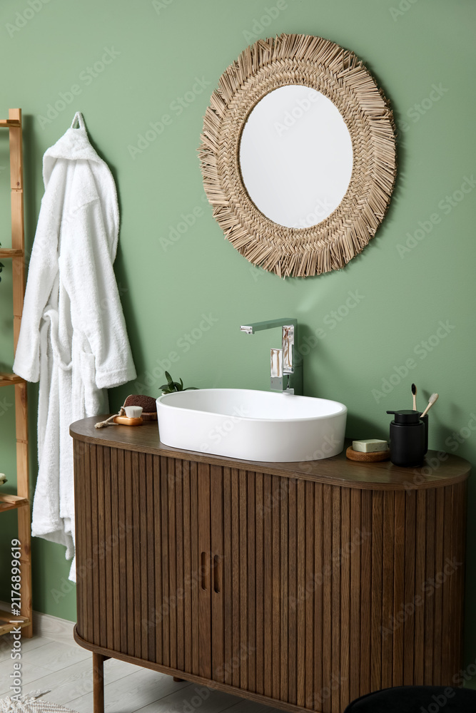 Obraz premium Modern sink with bath supplies on countertop and stylish mirror near green wall in bathroom