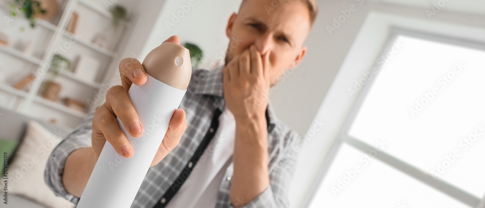 Obraz premium Bad odor and air freshener usage, man covering nose while spraying aerosol to remove unpleasant smell in home living room environment