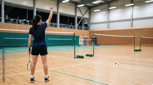 Young adult Asian female badminton player celebrating victory with fist raised in indoor court arena