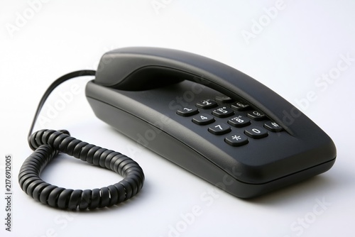 Black landline telephone with coiled cord on white