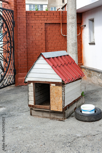 A doghouse on a concrete surface next to a brick wall and a metal fence.