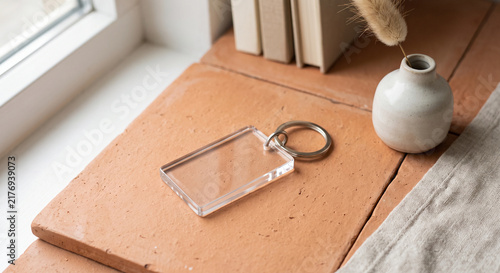 Transparent acrylic keychain blank on terracotta tile mockup closeup horizontal surface with miniature vase and books