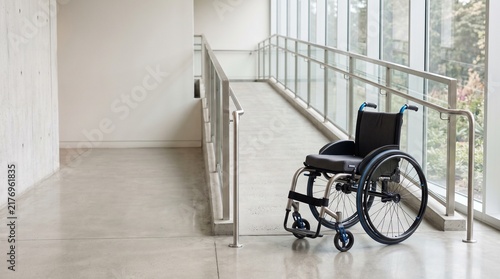 Manual wheelchair parked on a concrete ramp in a bright hallway