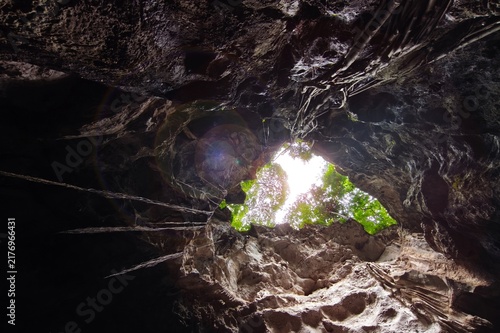 Low angle view of a dark cave exit with sunlight streaming into the cave shaft.