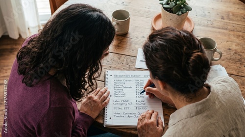 Two women reviewing renovation budget notes at wooden table