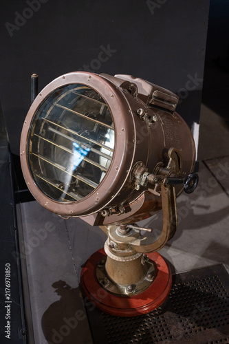 Vintage nautical signal light with louvered shutters mounted on a pedestal, indoor museum exhibit display.