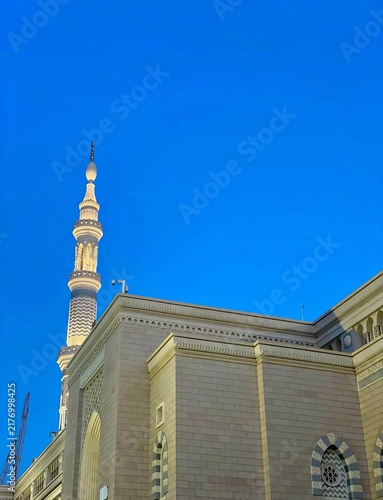 Quadro su tela Low angle shot of an illuminated minaret and stone facade of Al-Masjid an-Nabawi against a vibrant blue sky